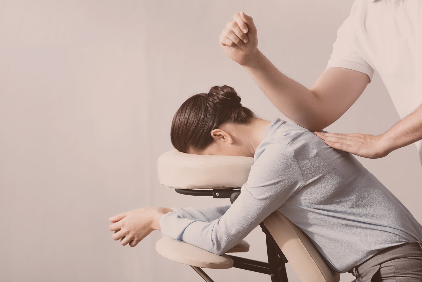 Side view of masseur massaging woman back with elbow, sitting on massage chair on white background